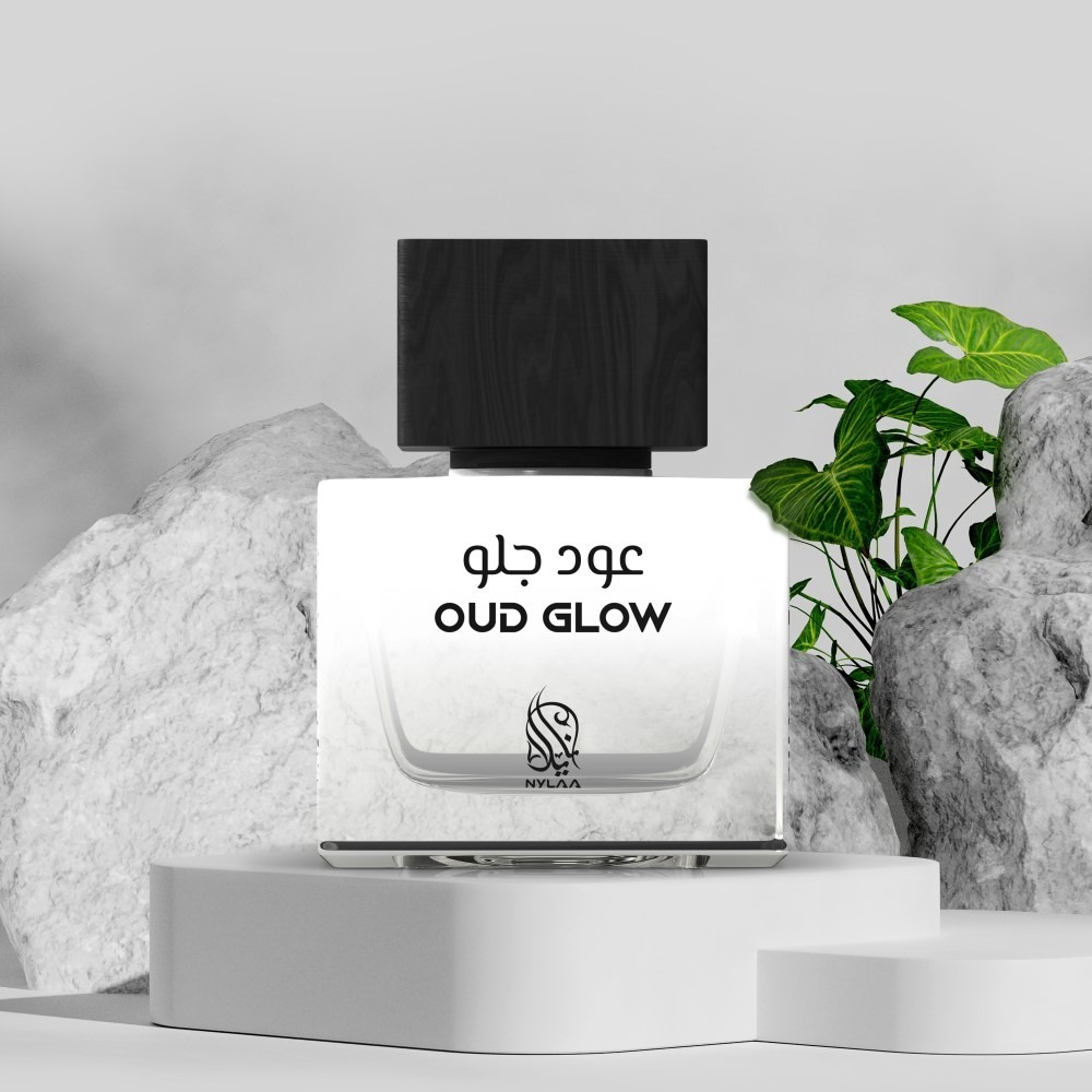 A black & grey perfume bottle from Nylaa by Savia Exclusive placed against white rocks & green leaves