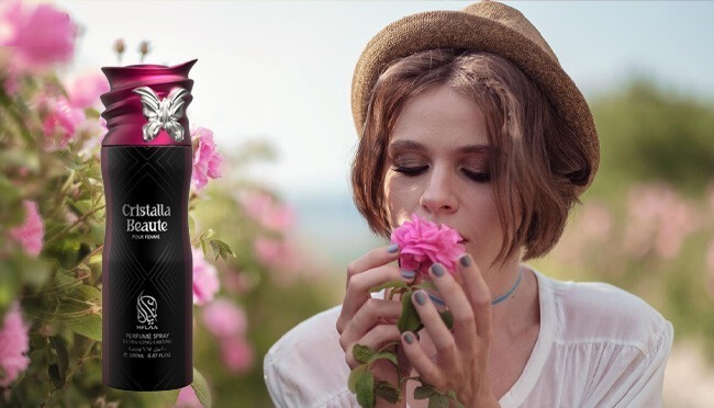 A woman wearing a white dress & brown hat smelling a pink flower