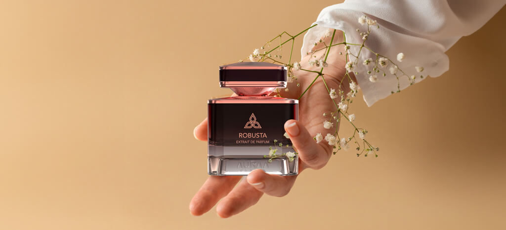 A maroon perfume bottle by Savia Exclusive in a hand with flowers