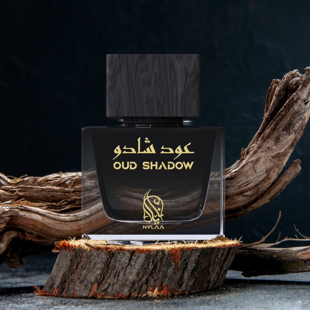 A grey & black perfume bottle from Nylaa by Savia Exclusive with a black cap placed on a brown oak platform with oak branches