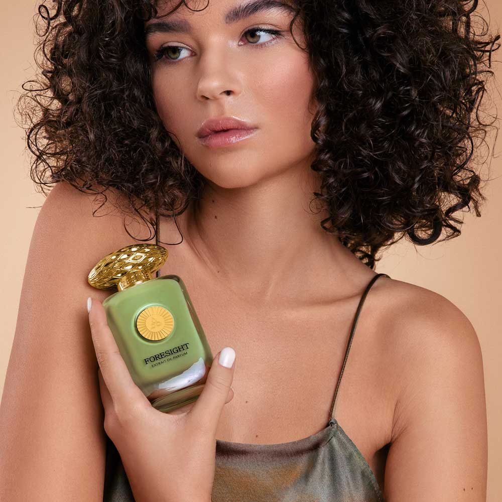 A woman with curly hair & glossy lips holding a perfume bottle