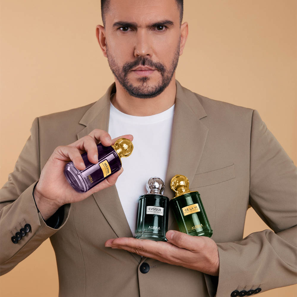 A man in a blazer holding 3 luxurt perfumes by Savia Exclusive