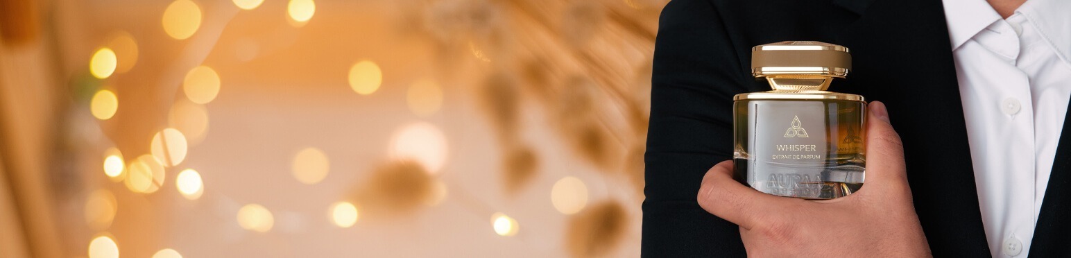 A man wearing a black suit holding a perfume bottle by Savia Exclusive with fairy lights in the background