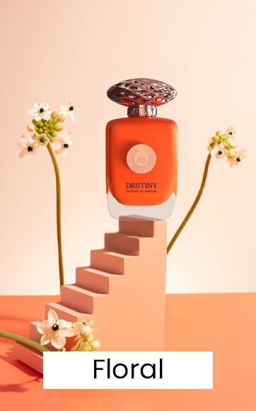 An orange perfume bottle by Savia Exclusive on pink stairs with a pink background & white flowers
